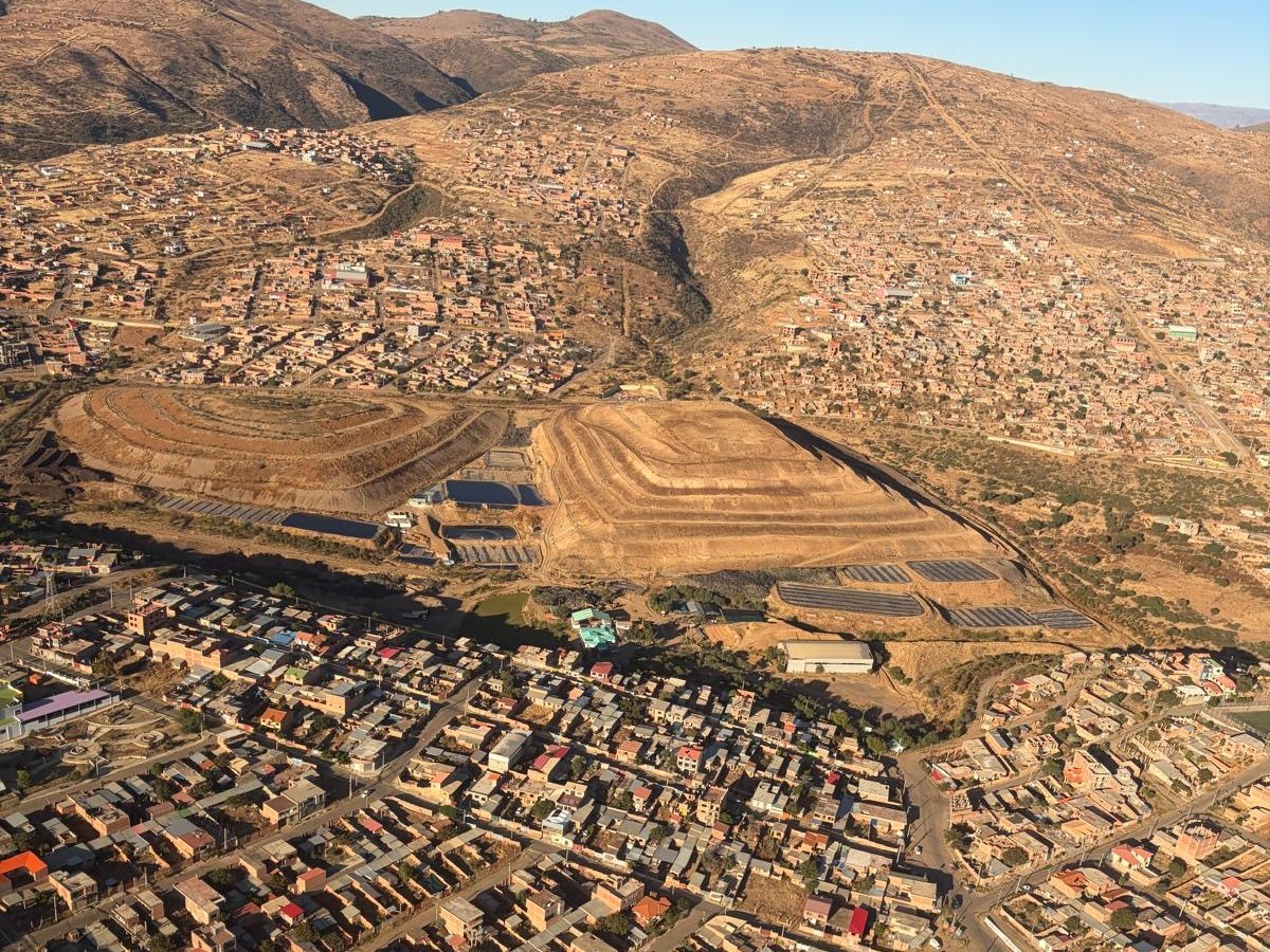 A city in a high Andean valley at first light, seen from the air: dry ridges above, rooftops filling the valley floor below